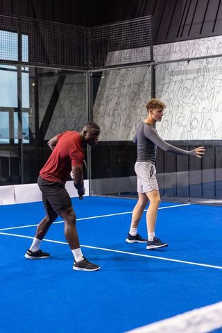 Diverse male athletes playing padel on blue indoor court showing ready stance sports training