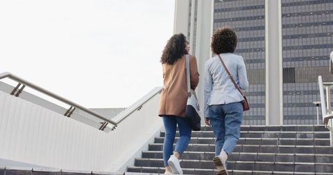 Young women walking up urban steps toward office tower in blazers carrying tote bags