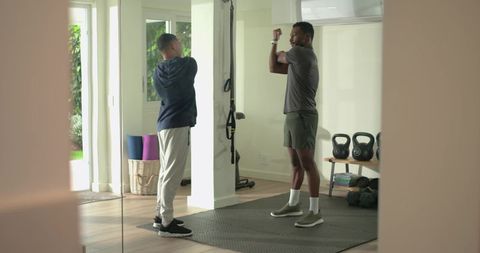 Diverse men stretching together in bright home gym with kettlebells, trx and mirror