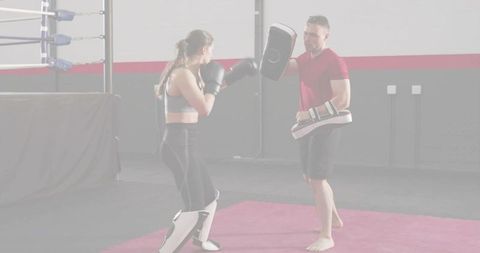Female boxer training with coach using focus mitts and shin guards in boxing gym