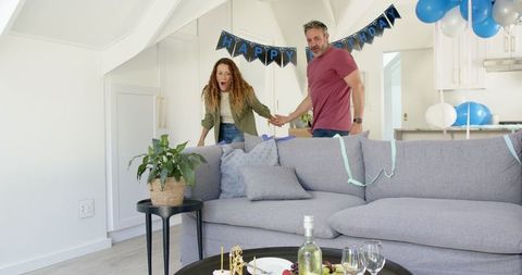 Surprised couple enjoying birthday celebration in decorated living room