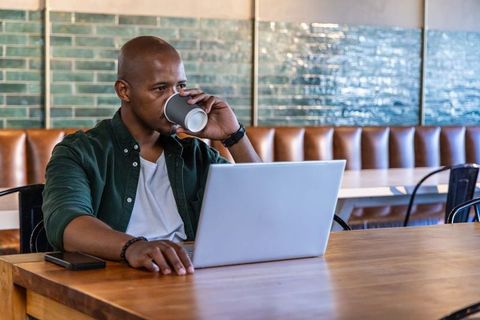 African american man working remotely in cafe, drinking coffee while using laptop