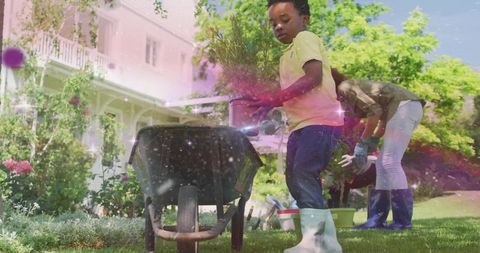 Child and parent gardening planting potted plants with wheelbarrow in sunny suburban yard