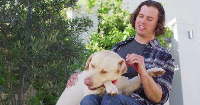 Man in a plaid shirt interacting with his Labrador retriever in an outdoor setting. Ideal for use in articles or advertisements about pet care, companionship, and outdoor activities. Perfect for veterinary services, pet food brands, and lifestyle blogs.