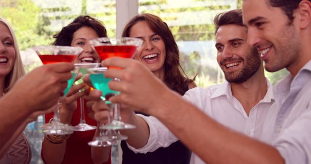 Group of friends celebrating together by raising cocktail glasses during a lively party. All participants are smiling and enjoying the moment. Useful for portraying social gatherings, nightlife, celebrations, and friendship.