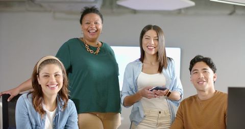 Diverse coworkers smiling and collaborating in modern office with smartphone and monitor