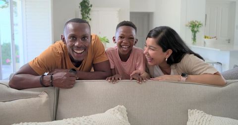 Sunlit family laughing together over beige sofa in modern cozy living room