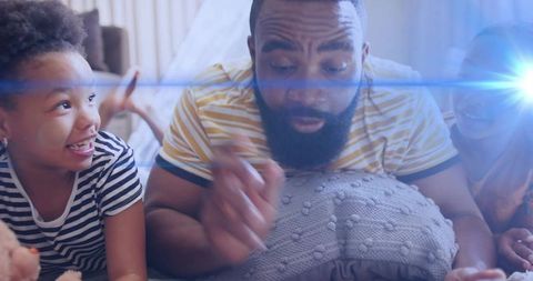 Father pointing and playing with children on bed, cozy family bonding with light flare