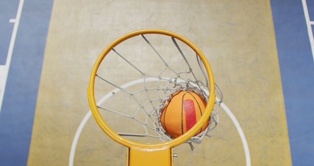 Top view of an orange basketball going through a hoop, capturing the moment of scoring. Ideal for sports-related content, motivational posters, basketball training materials, and sports event promotions.