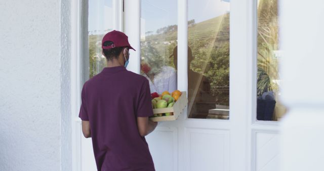 Worker delivering a crate of fresh produce to the front door of a home, emphasizing the convenience of modern grocery delivery services. Excellent for use in promotions of grocery apps, advertisements for delivery services, community aid programs, or articles related to the growing trend of home grocery deliveries.