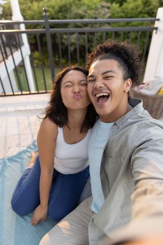 Young couple taking joyful balcony selfie with asian woman puckering and laughing
