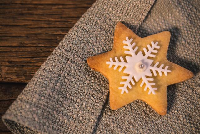 This image features a star-shaped gingerbread cookie decorated with white snowflake icing, placed on a textured fabric on a rustic wooden table. Ideal for holiday-themed promotions, festive recipe blogs, Christmas greeting cards, and seasonal advertisements.