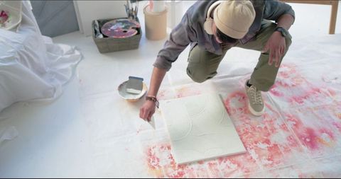 Indian artist crouching in studio applying textured paste with palette knife on canvas