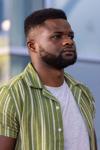 African man posing with trimmed beard and high-top fade wearing green striped shirt
