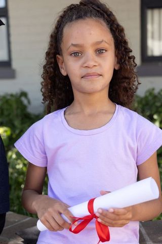 Young girl holding rolled diploma with red ribbon outdoor portrait celebrating achievement