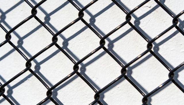 Black chain-link fence casting diamond lattice shadows across white stucco wall