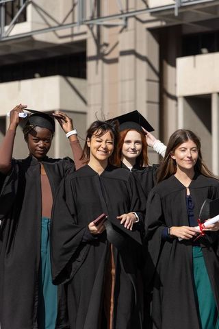 Diverse female graduates celebrating with mortarboards and diplomas at university plaza