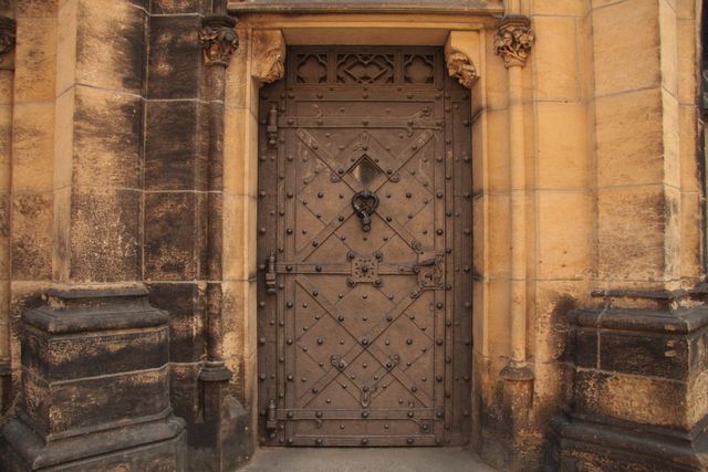 The image depicts an ancient wooden door reinforced with intricate iron rivets set in a thick stone wall. The detailed ironwork and weathered stone frame evoke a sense of history and old-world craftsmanship. This image is perfect for illustrating historical buildings, medieval architecture, and themes of antiquity. It can be used in educational materials, travel guides, and any projects related to heritage and old architecture.