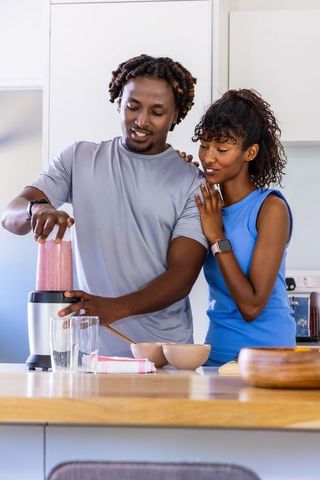 African american couple blending pink smoothie at modern kitchen island