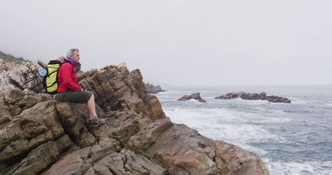 Senior Hiker Sitting on Rocky Shoreline Enjoying Sea View - Download Free Stock Images Pikwizard.com