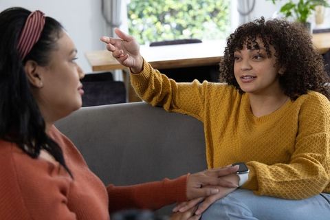 Two friends holding hands and talking on cozy sofa, intimate support and emotional connection
