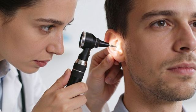 Female clinician examining male ear with otoscope during close-up ent checkup