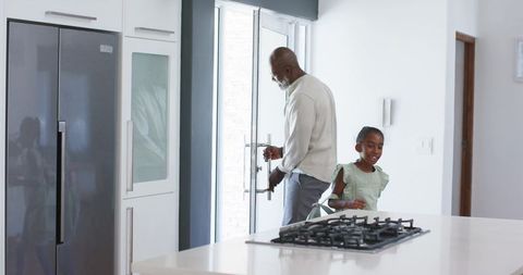 Senior african american father unlocking glass door while daughter laughing in kitchen