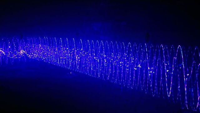 Electric blue helix light sculpture stretching across urban park nightscape with dotted led points