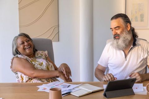 Mature colleagues laughing while reviewing tablet and color charts in bright minimalist office