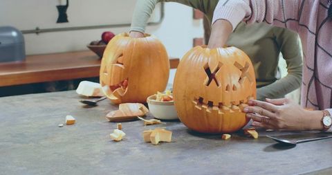 Women carving jack-o-lanterns on kitchen counter scooping pumpkin guts for autumn craft