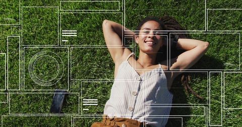Woman relaxing on grass with smartphone and digital interfaces