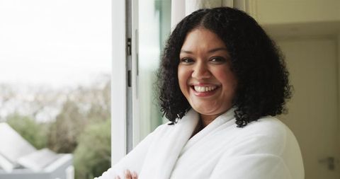 Smiling woman in white bathrobe relaxing by open sliding door enjoying morning light