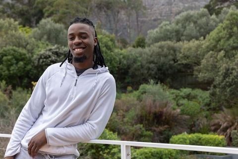 Smiling african american man leaning on balcony wearing hoodie amid lush terrace greenery