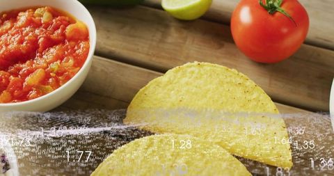 Folded corn taco shells showcasing chunky salsa, lime and tomato on rustic wooden plank