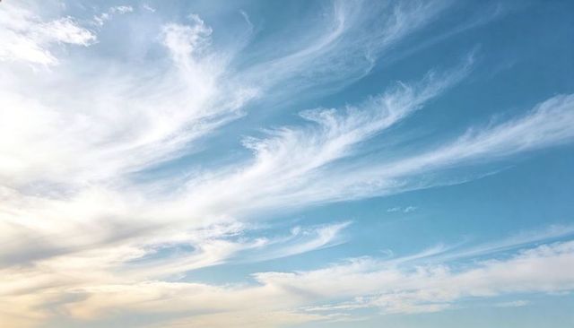 Wispy cirrus clouds sweeping across blue sky with warm-to-cool gradient