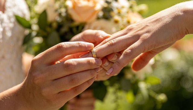 Sunlit garden wedding exchanging gold patterned ring closeup with rose bouquet and lace