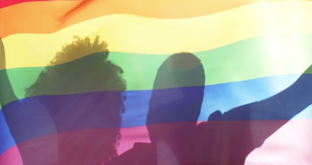 Diverse lesbian couple embracing and holding a rainbow flag outdoors. Togetherness, relationship, love, lgbtg awareness summer and nature, unaltered.