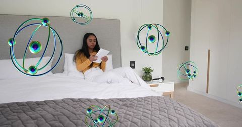 Young woman reading papers on bed with floating augmented-reality atomic orbitals