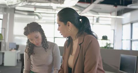 Multicultural female coworkers collaborating over data on monitors in bright modern office