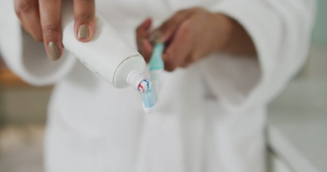 Hand squeezing toothpaste onto toothbrush in bathroom setting, representing morning routine and hygiene. Ideal for promoting dental care products or illustrating everyday hygiene habits.