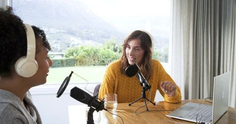 Two female podcast co-hosts recording conversational interview at bright home studio