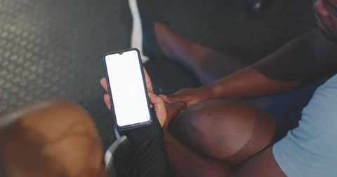 African men comparing workout plan on smartphone after gym session, sharing progress