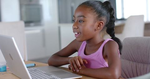 African American girl learning online using laptop at sunlit kitchen table