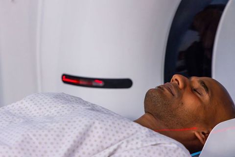 African american man lying in ct scanner receiving neck alignment with red laser, calm