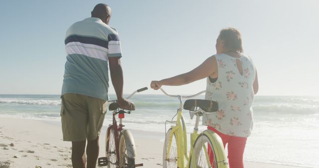 Senior couple enjoying a beachside walk while pushing their bicycles. Ideal for adverts focusing on active aging, healthy lifestyles, beach vacation promotions, and retirement plans. Symbolizes companionship, wellness, and the freedom of older age.
