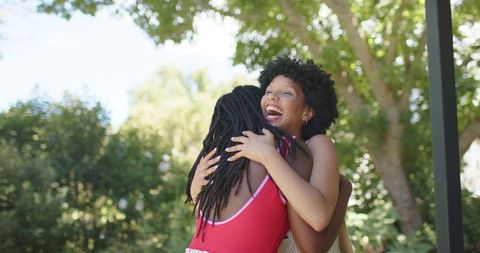 African american friends embracing and laughing in sunny park among green trees, summer