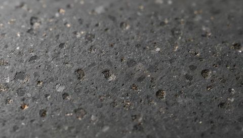 Dark volcanic rock surface showing porous circular pits and mineral fleck macro texture