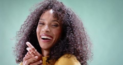 Joyful African American Woman Smiling with Curly Hair and Rings Wearing Mustard Yellow Top