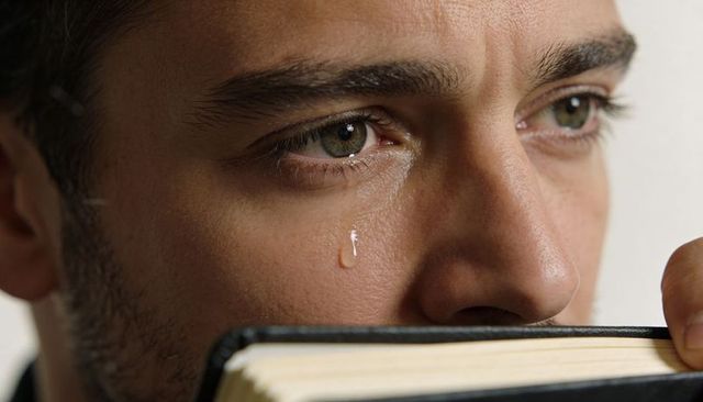 Man shedding tear while holding hardcover journal near mouth closeup emotional portrait
