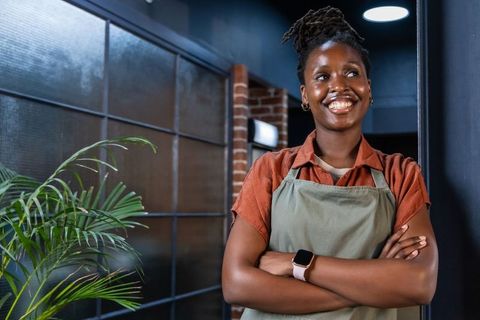 Confident african american barista smiling with arms crossed in modern cozy cafe interior